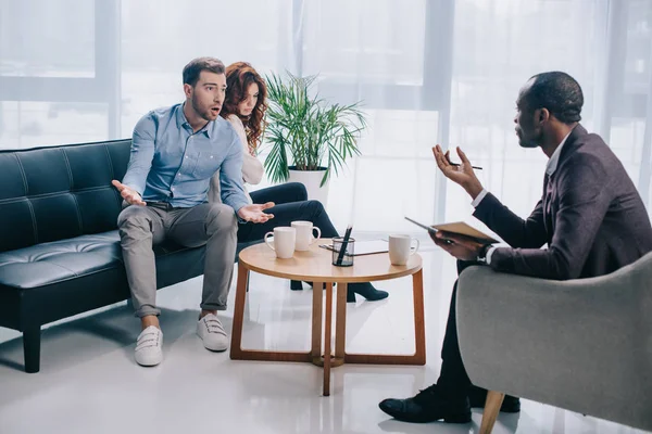 Wütender junger Mann mit Freundin sitzt auf Sofa und streitet mit Berater — Stockfoto