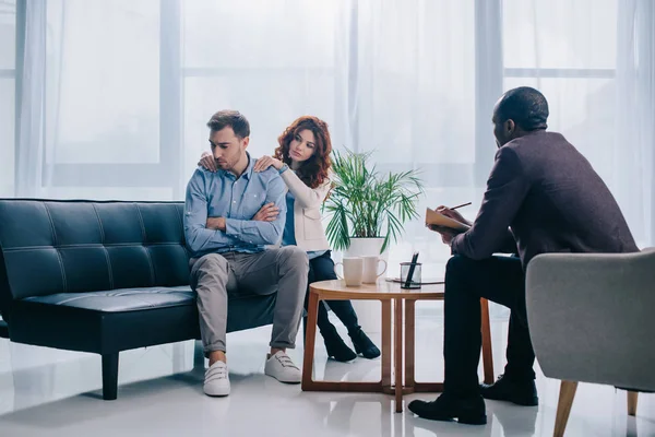 Counselor sitting in armchair while young woman doing massage to boyfriend — Stock Photo