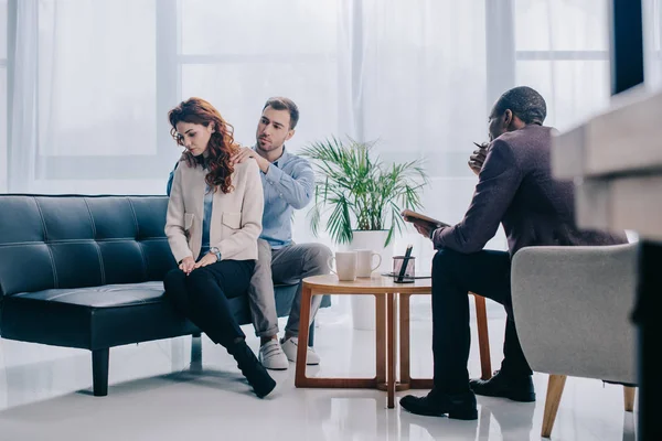 Consejero afroamericano sentado en sillón mientras hombre haciendo masaje a novia - foto de stock