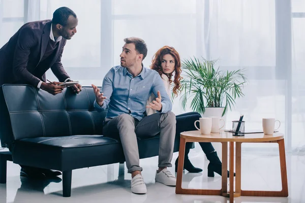 Counselor with clipboard talking to upset couple sitting on couch — Stock Photo