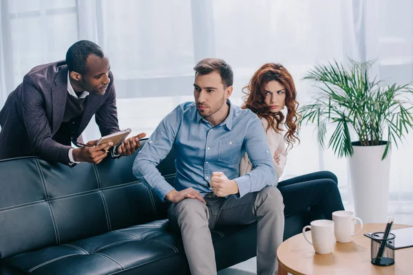 Counselor with clipboard talking to young couple sitting on sofa — Stock Photo