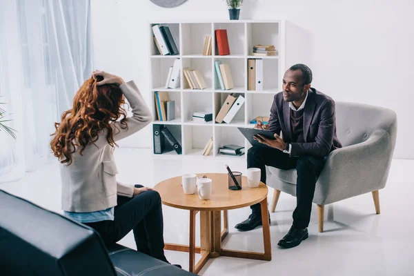 Psiquiatra afro-americano sentado em poltrona e conversando com paciente do sexo feminino — Stock Photo