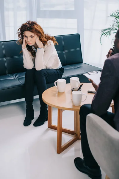 Femme bouleversée assise sur le canapé et psychiatre assis près — Photo de stock