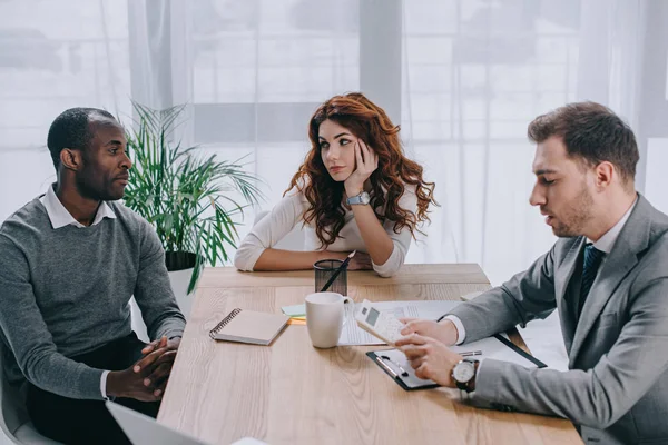 Conseiller financier effectuant le calcul pendant que les partenaires commerciaux sont assis à table — Photo de stock