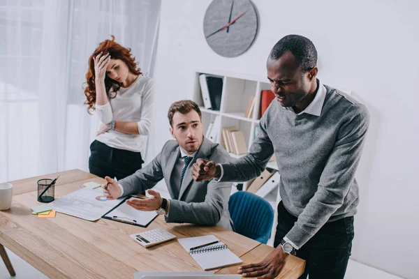 Angry businessman with upset businesswoman and financial adviser sitting at table — Stock Photo