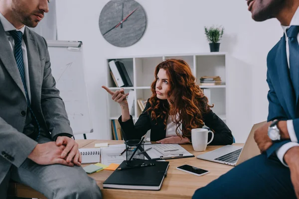 Cropped view of two businessmen sitting on table and manager pointing by finger — Stock Photo