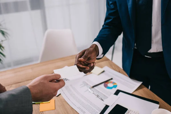 Cropped view of businessman giving visit card to african american partner — Stock Photo