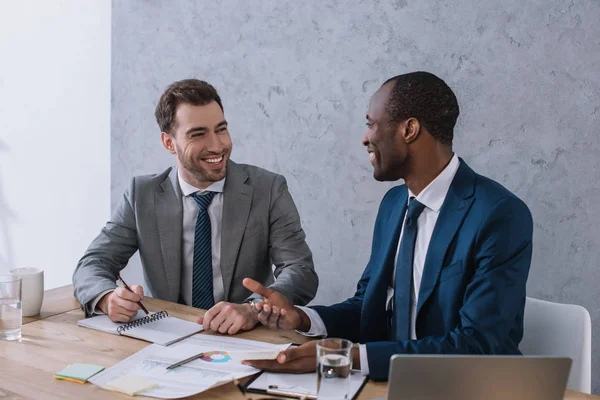 Des hommes d'affaires souriants travaillant à table avec des papiers au bureau — Photo de stock