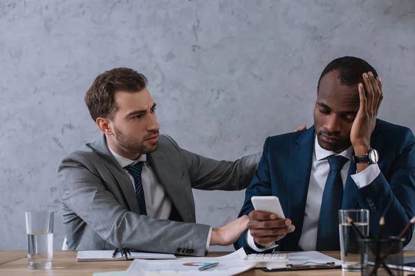 Jovem empresário elegante animando parceiro chateado com smartphone na mão — Fotografia de Stock