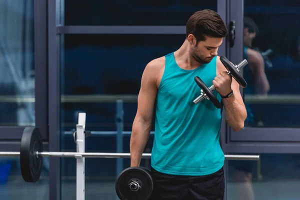 Мускулистый спортсмен тренируется с гантелями в тренажерном зале — стоковое фото