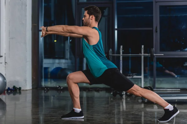 Sportsman squatting and stretching legs in gym — Stock Photo