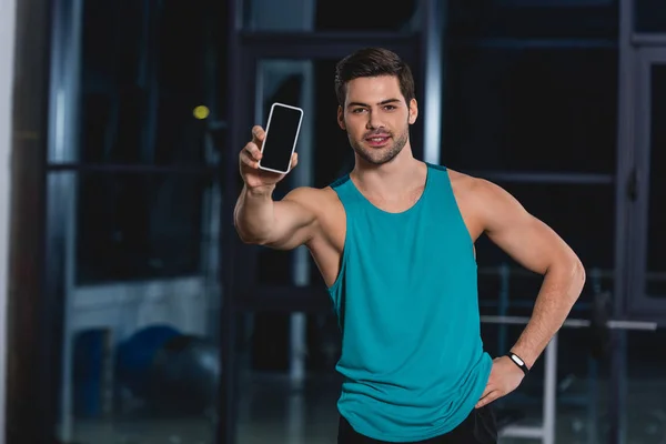 Apuesto deportista mostrando teléfono inteligente con pantalla en blanco - foto de stock