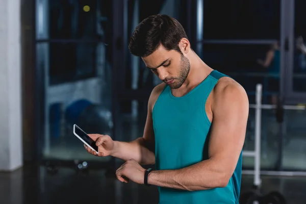 Sportsman using fitness tracker and smartphone in gym — Stock Photo