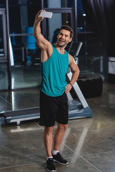 Deportista alegre tomar selfie en el teléfono inteligente en el gimnasio con cinta de correr - foto de stock