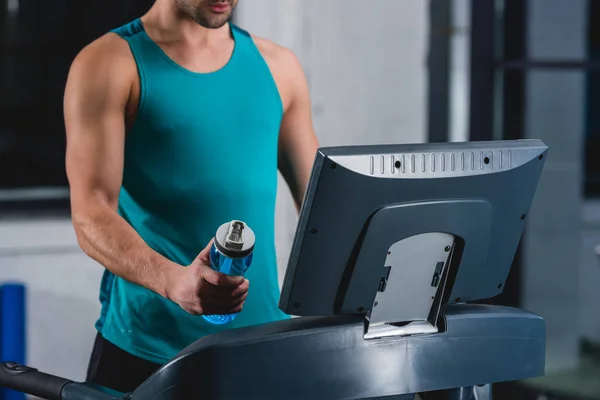 Vista ritagliata di sportivo con bottiglia di allenamento sportivo sul tapis roulant in palestra — Foto stock