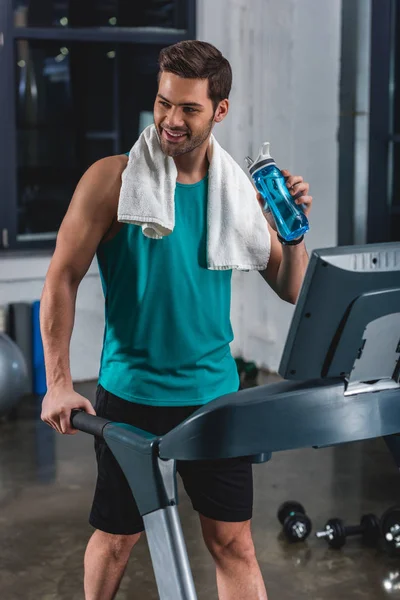 Smiling tired sportsman with towel and sport bottle training on treadmill in gym — Stock Photo