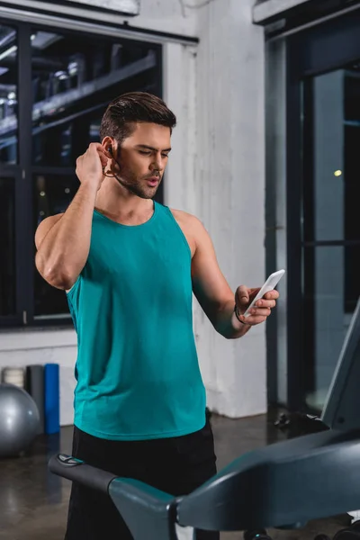 Desportista ouvir música com fones de ouvido e smartphone enquanto se exercita em esteira na academia — Fotografia de Stock