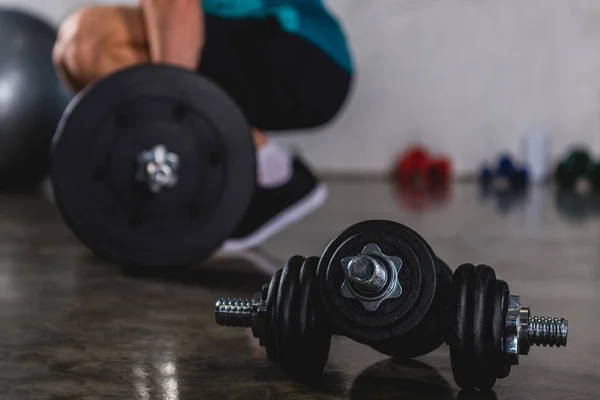 Sportsman training with barbell, dumbbells lying on floor on foreground — Stock Photo