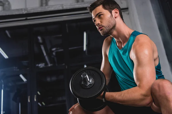 Muscular sportsman training with dumbbell in sports hall — Stock Photo
