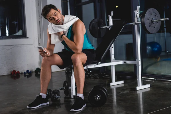 Sweaty sportsman with towel resting and using smartphone in gym — Stock Photo