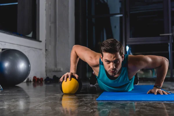 Sportsman doing push ups with medicine ball on yoga mat in gym — Stock Photo