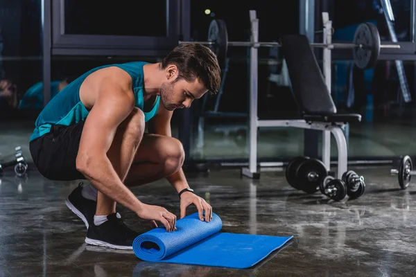 Sportsman rolling up yoga mat in sports center — Stock Photo