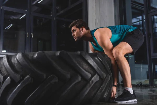 Sportsman lifting tire during cross training in sports center — Stock Photo