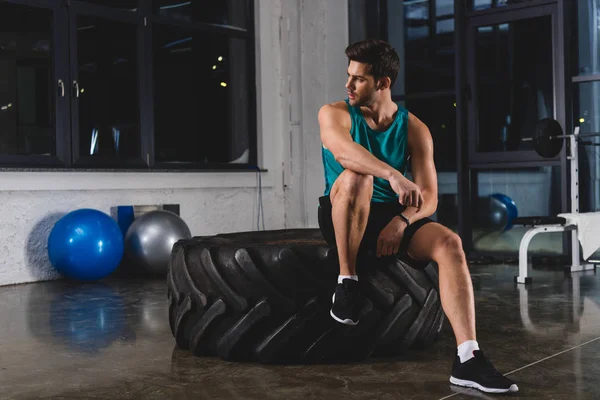 Sportsman sitting on tire in sports center — Stock Photo