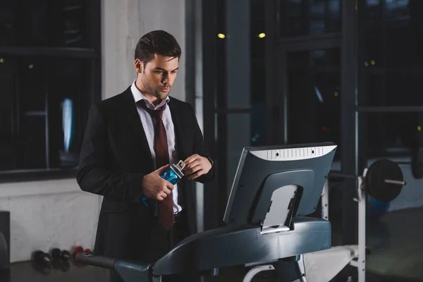 Businessman in suit training on treadmill with bottle of water in sports center — Stock Photo