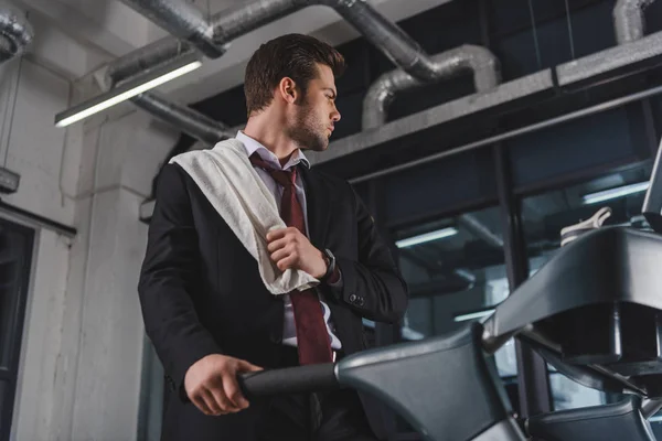 Tired businessman with towel training on treadmill in sports hall — Stock Photo