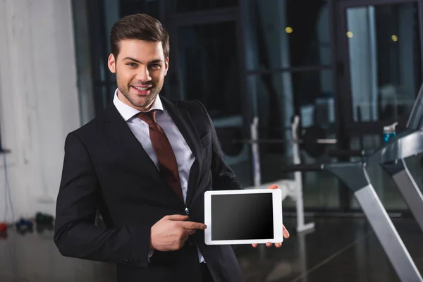 Smiling businessman in suit pointing at digital tablet in sports center — Stock Photo
