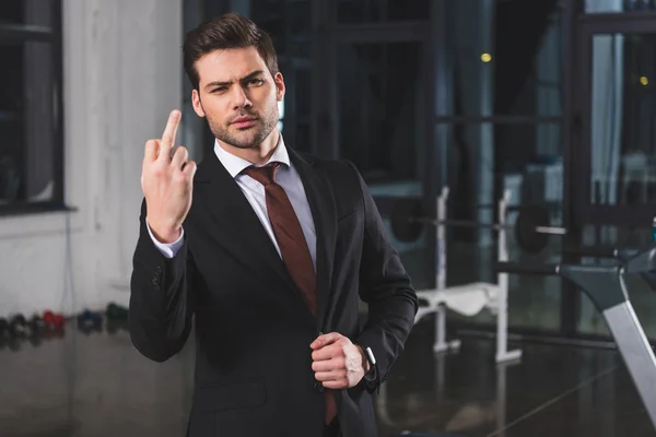 Businessman in formal wear showing middle finger in sports center — Stock Photo