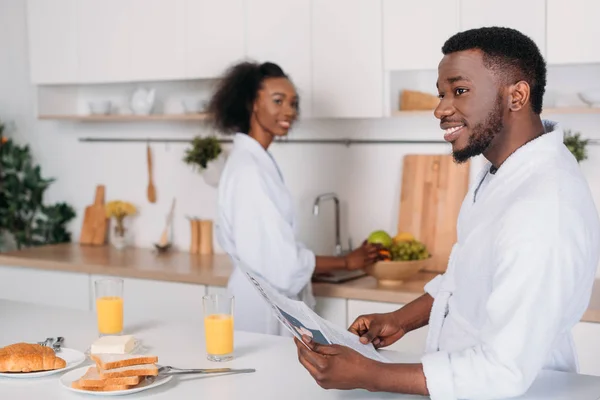 Uomo afroamericano con giornale e fidanzata in piedi dietro — Foto stock