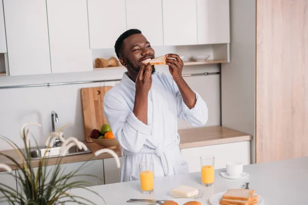 Jovem afro-americano comendo torradas na cozinha — Fotografia de Stock
