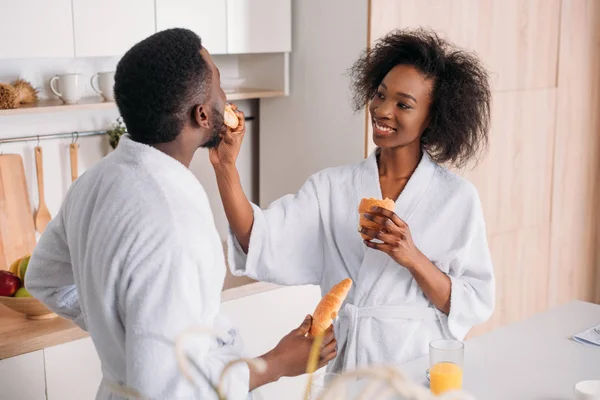Africano americano mujer alimentación novio por croissant en cocina - foto de stock
