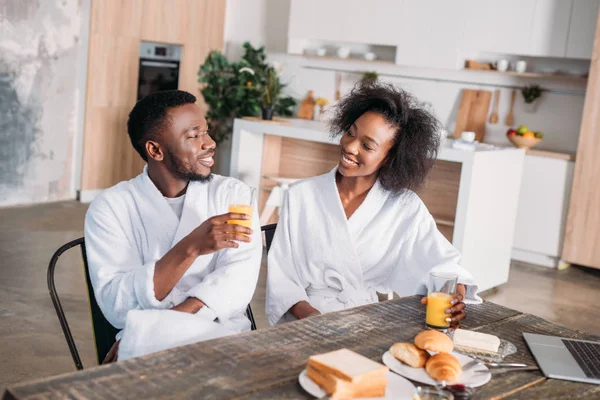 Casal sorridente sentado à mesa com café da manhã e laptop na cozinha — Fotografia de Stock