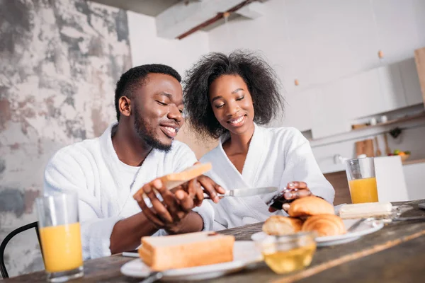 Coppia sorridente che stende marmellata su pane tostato a tavola con colazione — Foto stock