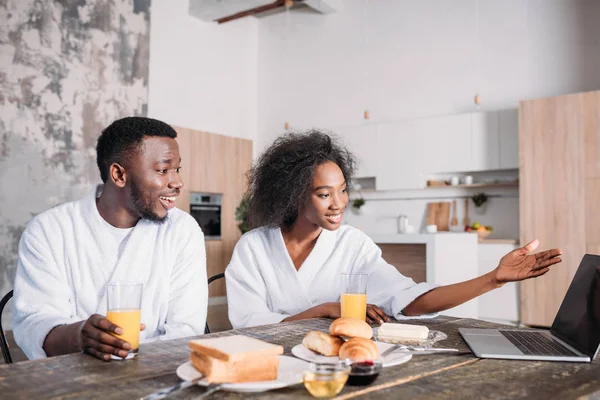 Pareja afroamericana joven sentada a la mesa con portátil y desayuno - foto de stock