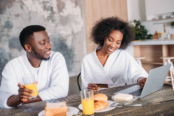 Africano casal americano tomando café da manhã e fazendo compras on-line na cozinha — Stock Photo