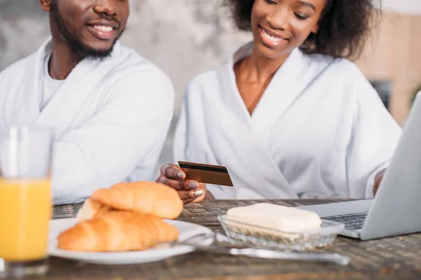 Imagem recortada de jovem casal sorrindo tomando café da manhã e fazendo compras on-line com cartão de crédito — Fotografia de Stock