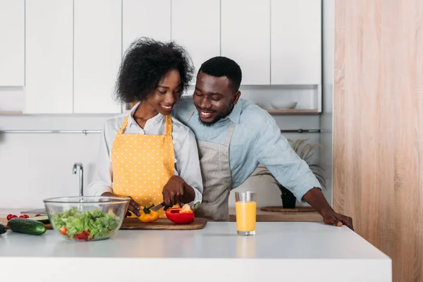 Pareja afroamericana en delantales de pie a la mesa y cocinando - foto de stock