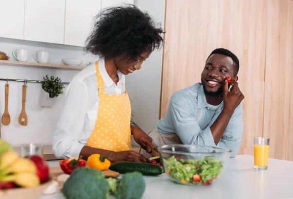 Souriant couple afro-américain dans des tabliers cuisine dans la cuisine — Photo de stock
