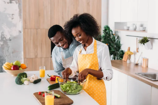 Smiling woman mixing salad in bowl while boyfriend standing near — Stock Photo