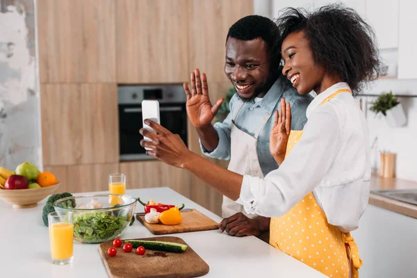 Sorrindo casal afro-americano em aventais tomando selfie na cozinha — Fotografia de Stock