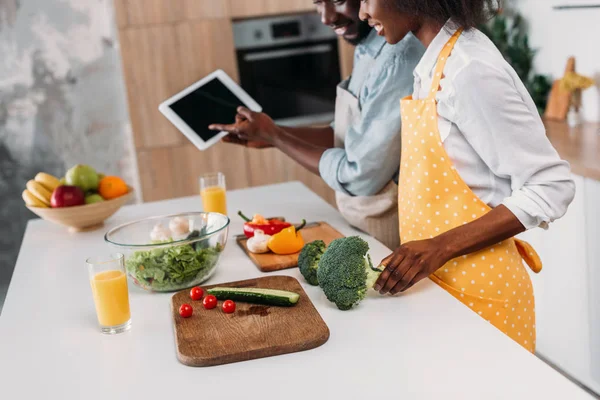 Paar schaut sich Rezept auf digitalem Tablet an, während es mit Gemüse am Tisch steht — Stockfoto