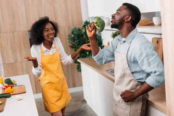 Young man depicting singing on broccoli while smiling girlfriend standing near — Stock Photo