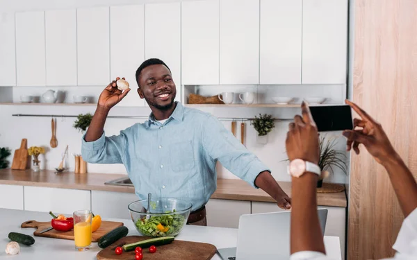 Cropped image of woman taking photo of boyfriend with mushroom in hand — Stock Photo