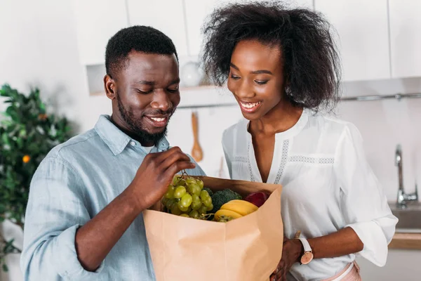 Joven pareja afroamericana sosteniendo bolsa de papel con uvas y plátanos - foto de stock