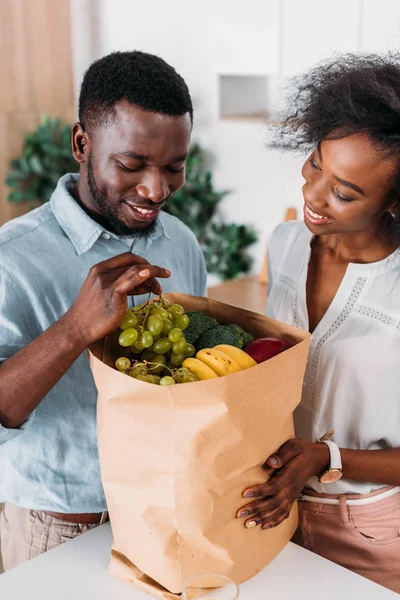 Young couple taking out grapes from paper bag with fruits — Stock Photo