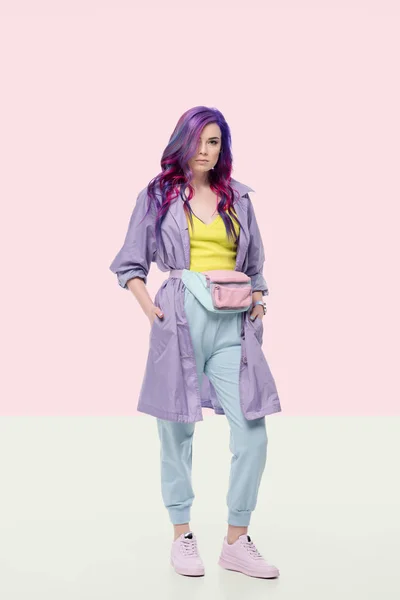 Attractive young woman in purple trench coat with waist pack on creative background — Stock Photo